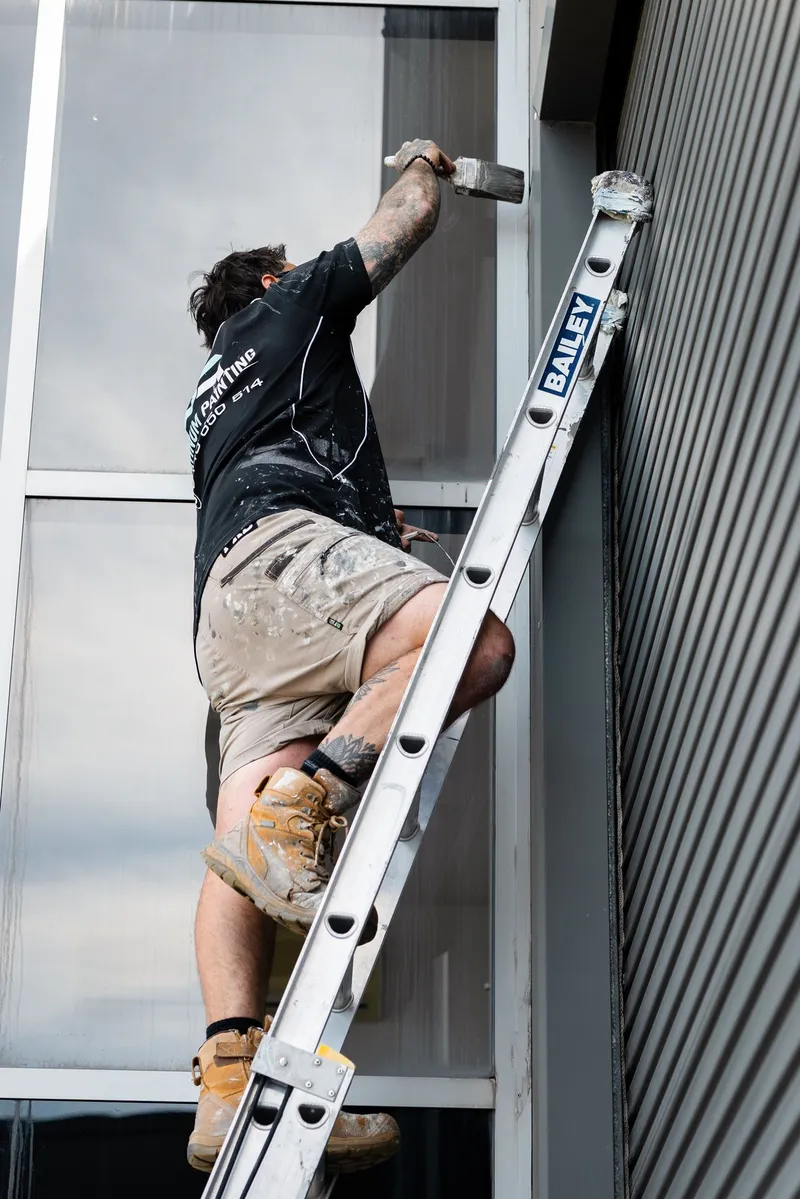 Painter working from a ladder on a commercial exterior
